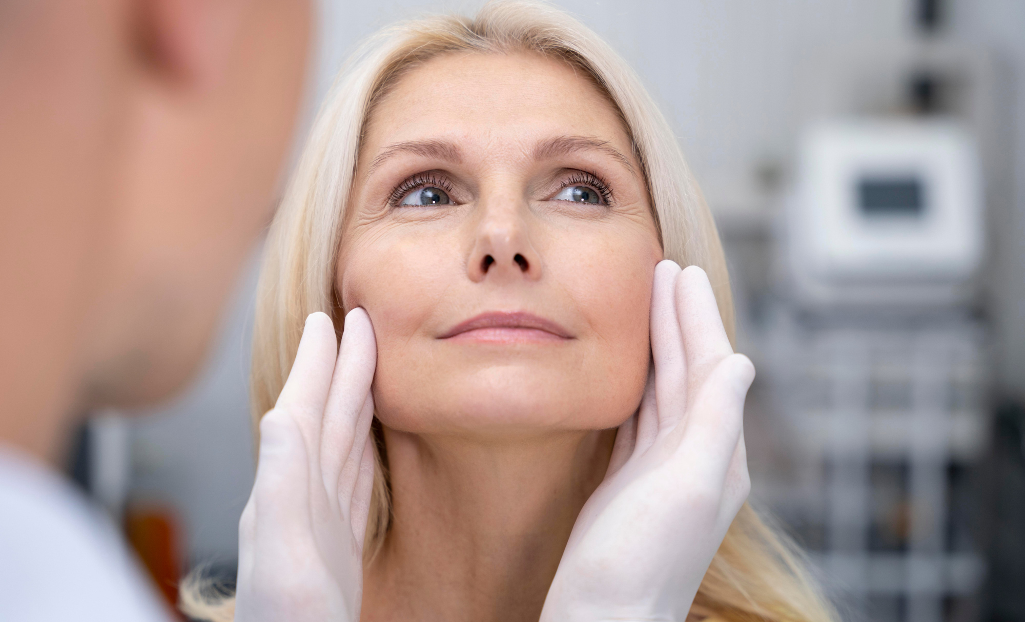 Provider's gloved hands hold woman's face that's been rejuvenated by laser treatment in Dallas.