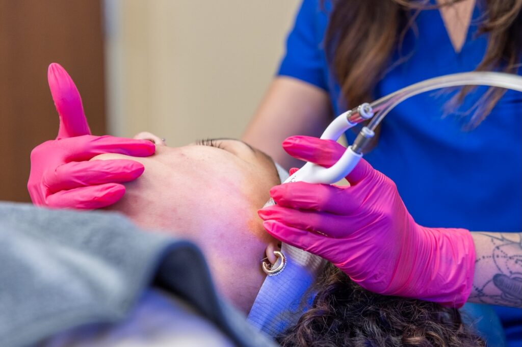 A provider glides the DiamondGlow handpiece over a patient's skin during a facial near Durant.